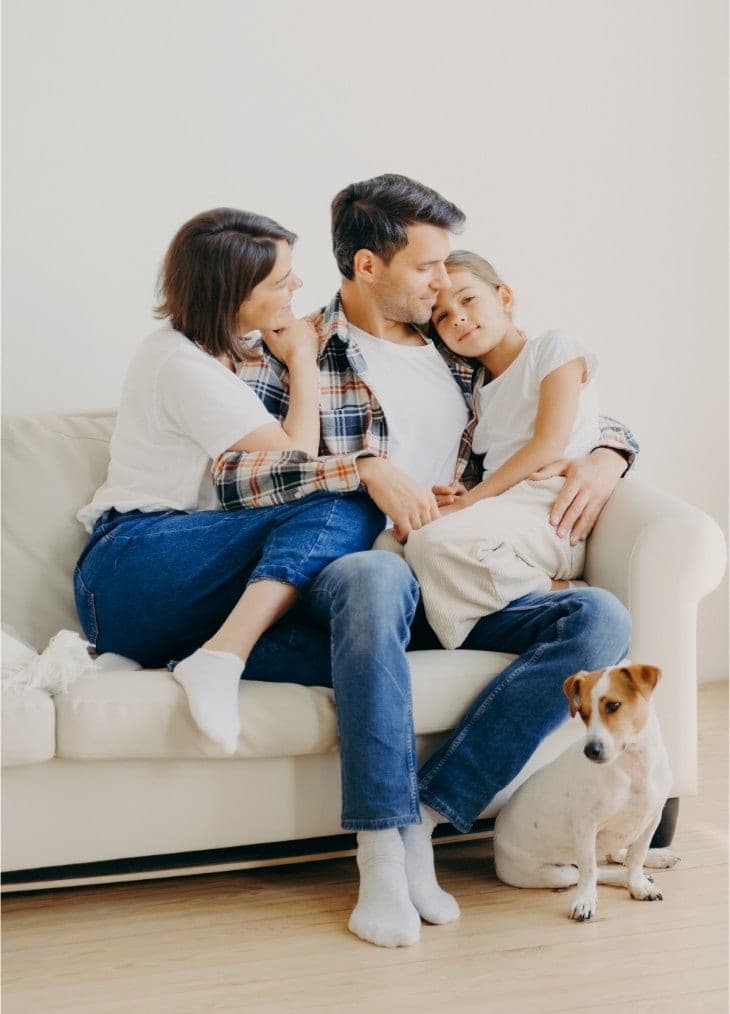 Una familia sentada junta en un sofá de su sala con su perro al lado